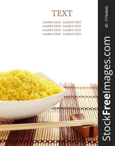 Boiled yellow rice and a white plate beside lie wooden sticks. Plate stands on a wooden mat. Isolated on a white background. Boiled yellow rice and a white plate beside lie wooden sticks. Plate stands on a wooden mat. Isolated on a white background