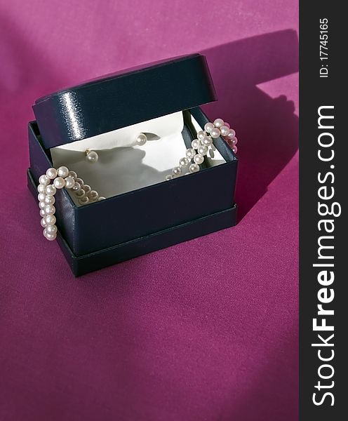 Box with stand of pearls and pearl earrings with shadows on a reddish textile