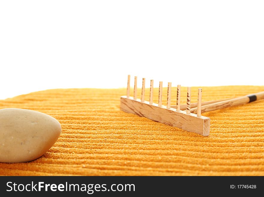 On the golden (orange) sand with wooden rakes made strips. Beside these wooden rakes. Rake in Zen Garden taken closeup