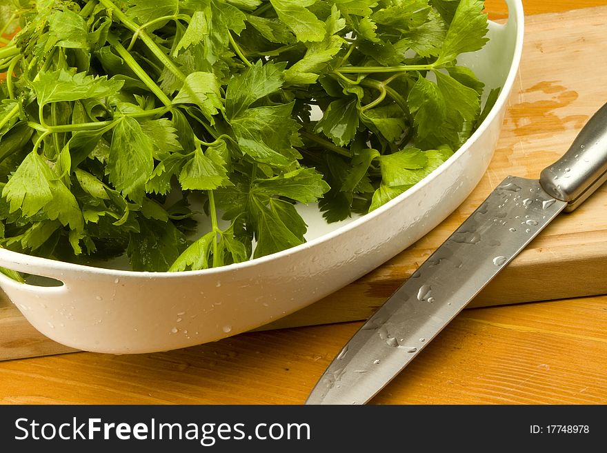 Freshly cut celery leaves in a white bowl on a wooden table with a cutting knife. Freshly cut celery leaves in a white bowl on a wooden table with a cutting knife