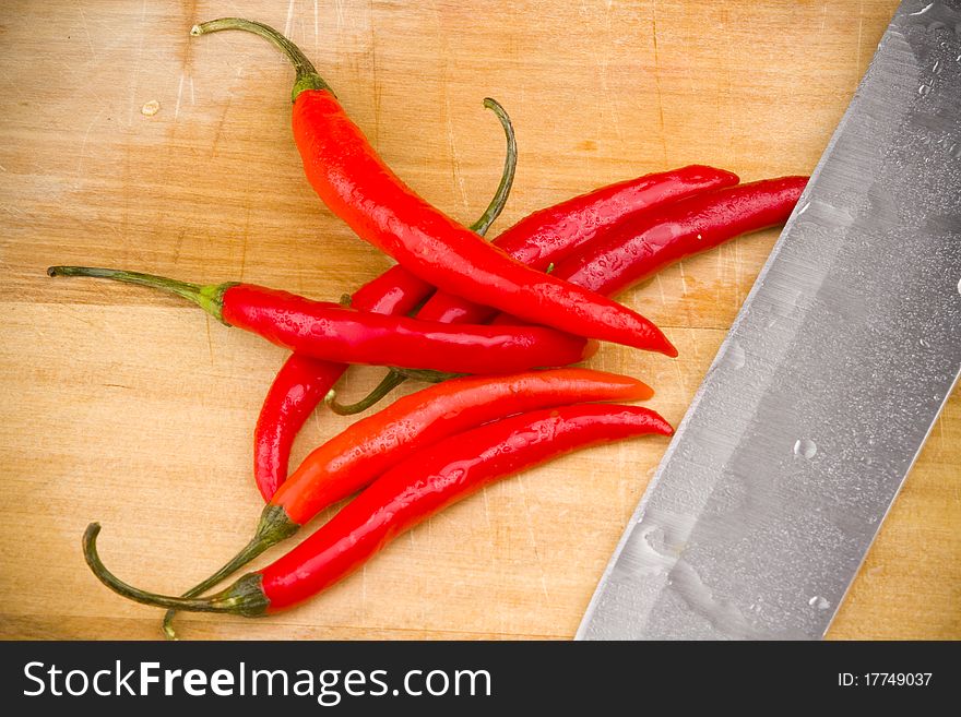 A bunch of red chili peppers on a wooden cutting board with a knife