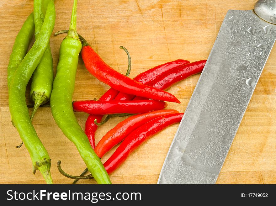 A bunch of red and green spicy chili peppers on a wooden cutting board with a knife