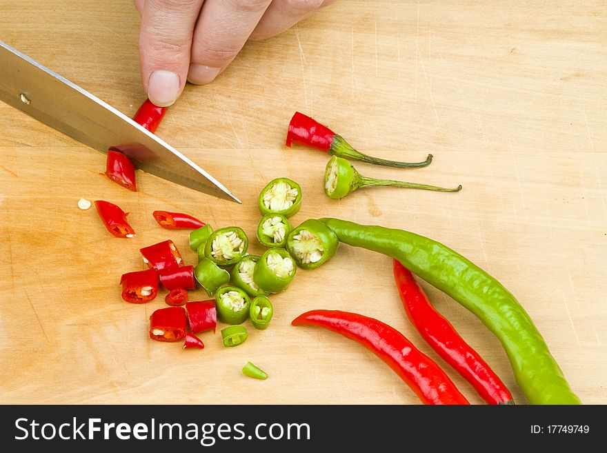 Person cutting a bunch of red and green spicy chili peppers on a wooden cutting board with a knife. Person cutting a bunch of red and green spicy chili peppers on a wooden cutting board with a knife