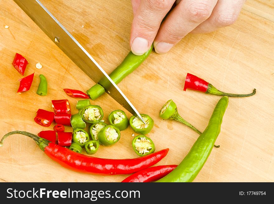 Person cutting a bunch of red and green spicy chili peppers on a wooden cutting board with a knife. Person cutting a bunch of red and green spicy chili peppers on a wooden cutting board with a knife