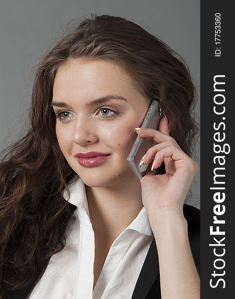 The young beautiful girl in a white blouse and a black jacket speaks by phone. The young beautiful girl in a white blouse and a black jacket speaks by phone