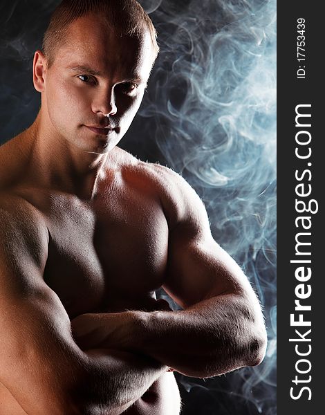 Young sporty man over Smoke. Muscles, a close up