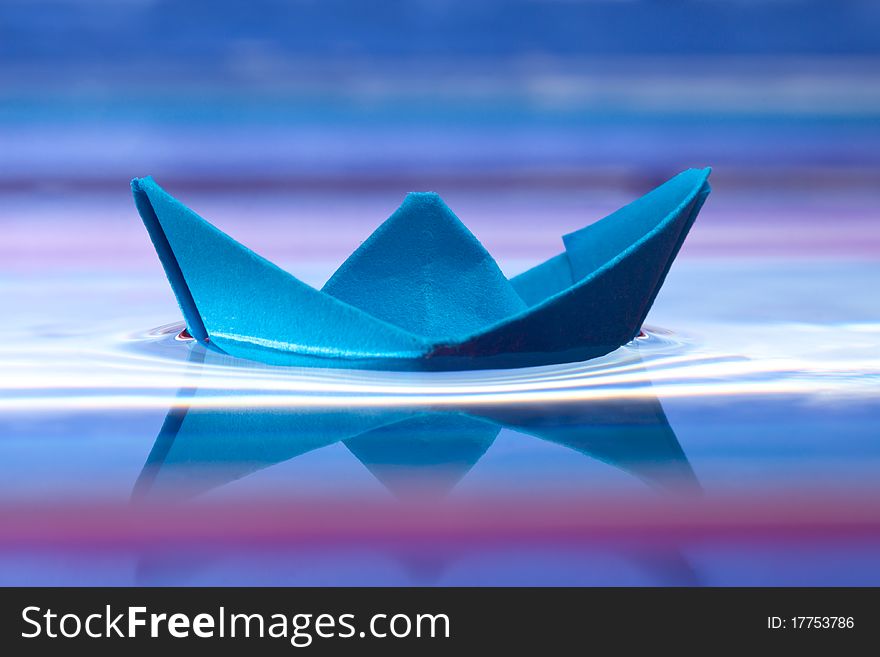 Blue paper boat and reflection on water, beautiful purple background