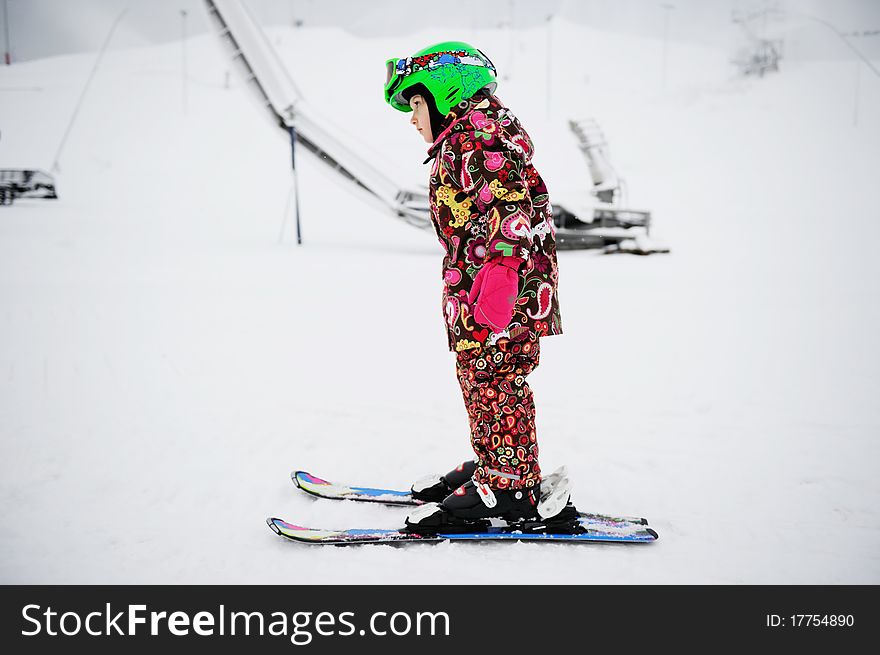Little girl in colorful snowsuit and green helmet on Alpine ski. Little girl in colorful snowsuit and green helmet on Alpine ski