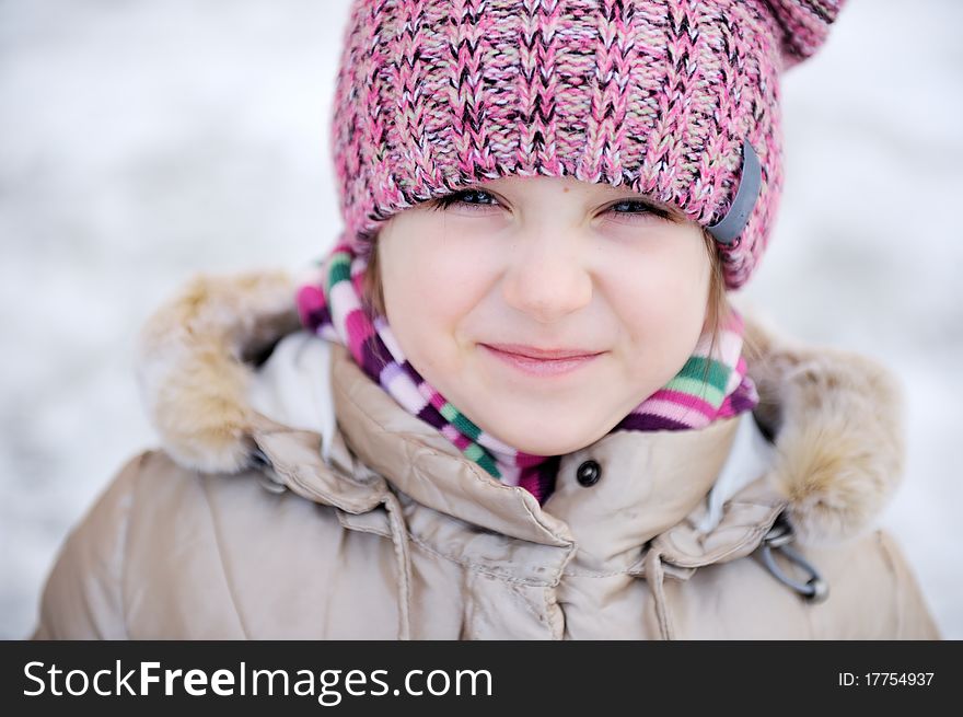 Winter portrait of adorable small girl with blue eyes in pink hat looks into the camera