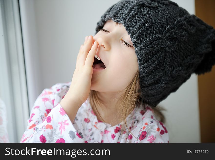 Adorable little kid girl with blue eyes in dark grey knit hat looks into the window. Adorable little kid girl with blue eyes in dark grey knit hat looks into the window