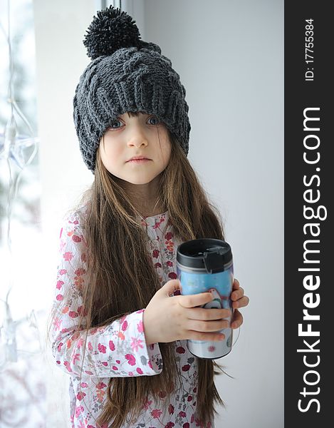 Adorable little kid girl with blue eyes in dark grey knit hat with cup. Adorable little kid girl with blue eyes in dark grey knit hat with cup