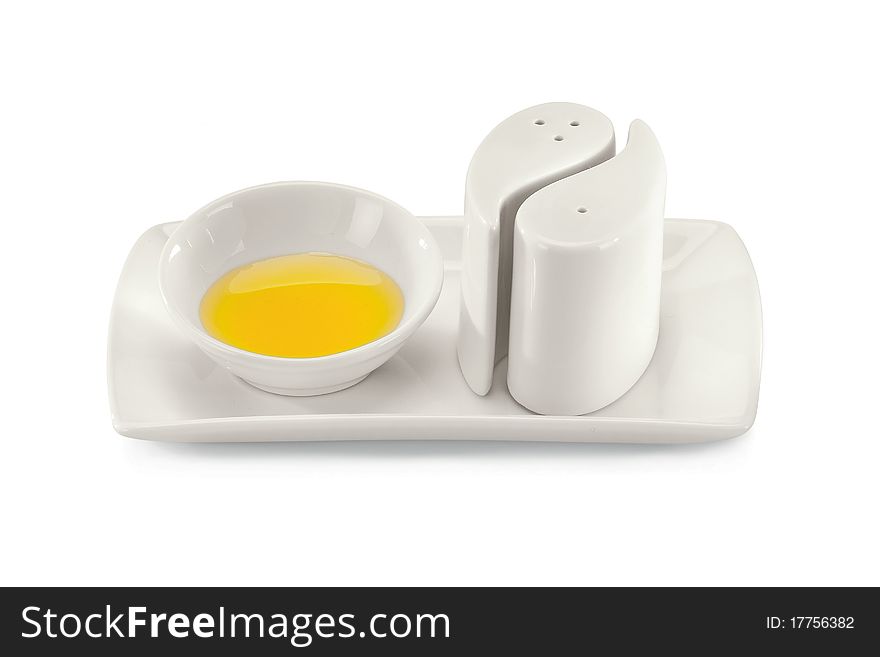 Yellow sauce in a bowl with black pepper pots isolated on a white background.
