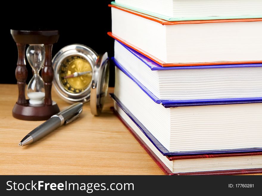 Pile of books, pen and hourglass on black background