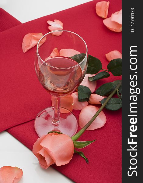 Glass of red wine with red table cloth and pink rose on on white background.