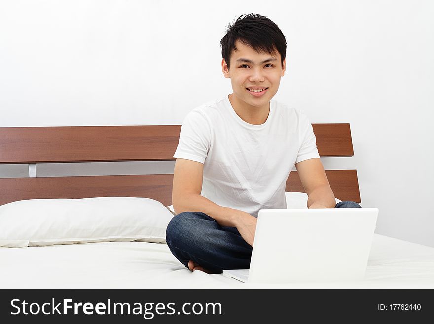 An Asian man on a bed with his laptop. An Asian man on a bed with his laptop