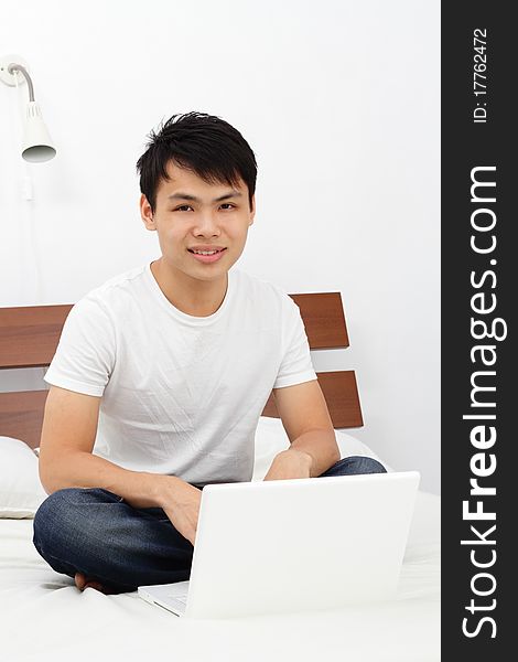 An Asian man on a bed with his laptop. An Asian man on a bed with his laptop