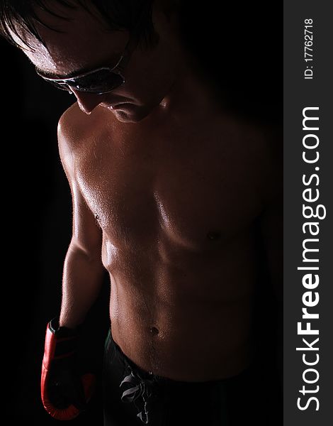 Sweated out model stands against a black background with boxing gloves on and shades. Sweated out model stands against a black background with boxing gloves on and shades