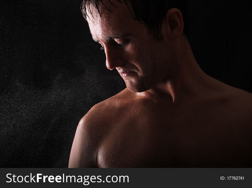 Male model standing against a black background with light shining in his face. water is also sprayed in the face of the model. Male model standing against a black background with light shining in his face. water is also sprayed in the face of the model