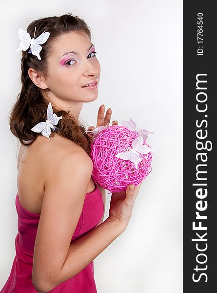 Sideview of young smiling woman with butterflies in her hair and pink make-up holding a pink sphere in her hands. Sideview of young smiling woman with butterflies in her hair and pink make-up holding a pink sphere in her hands