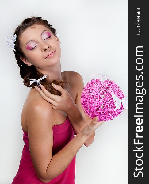 young woman with butterflies in her hair and pink make-up holding a pink sphere in her hands. young woman with butterflies in her hair and pink make-up holding a pink sphere in her hands