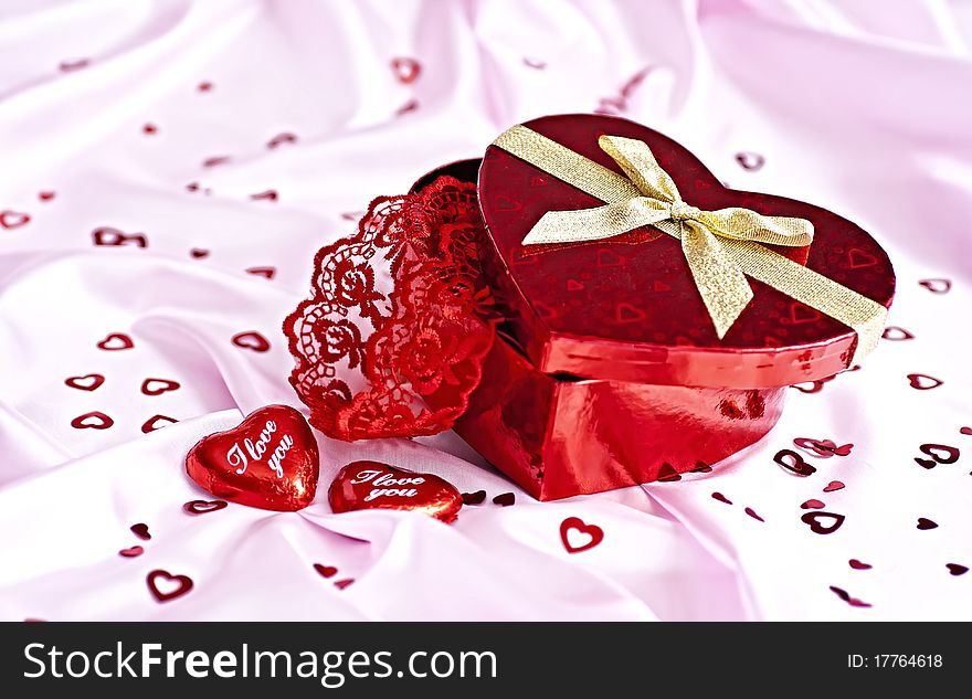 Pink bedding, gift box heart-shaped chocolate candy with the words I Love You and a lot of small distributed hearts. Surprise to the woman. Pink bedding, gift box heart-shaped chocolate candy with the words I Love You and a lot of small distributed hearts. Surprise to the woman.