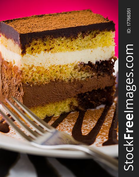 Creamy chocolate mousse cake on a white plate with a pink background. Added vignetting and very shallow depth of field.