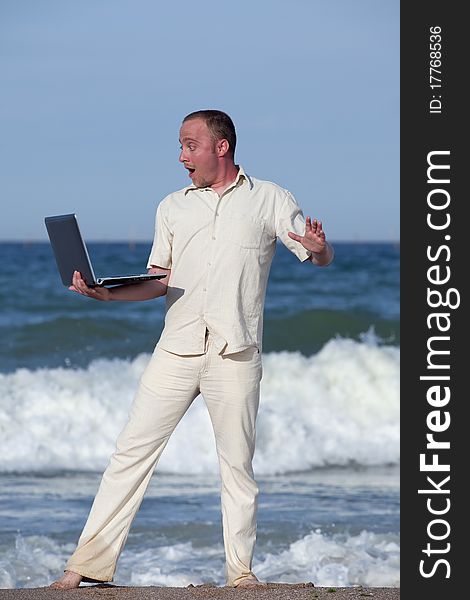 Young businessman at the beach with his laptop happy about success. Young businessman at the beach with his laptop happy about success