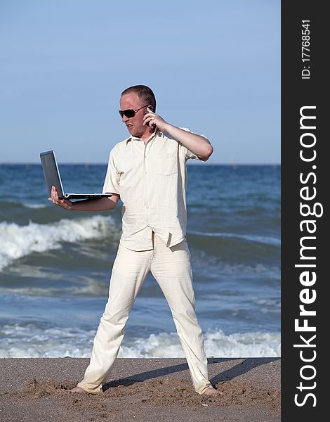 Angry man punching laptop at the beach