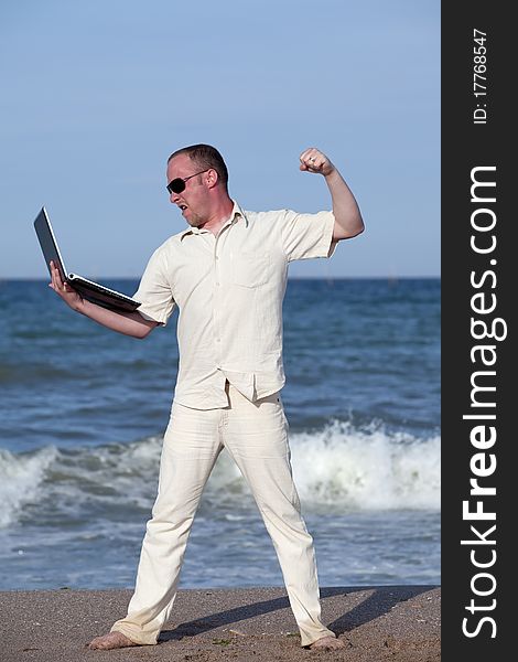 Angry man punching laptop at the beach