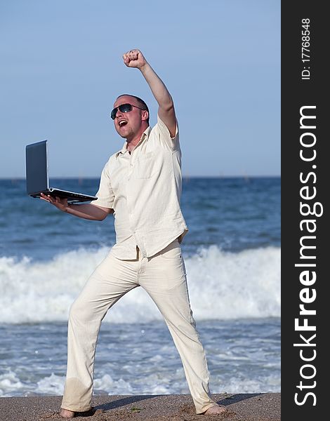 Young businessman at the beach with his laptop happy about success. Young businessman at the beach with his laptop happy about success