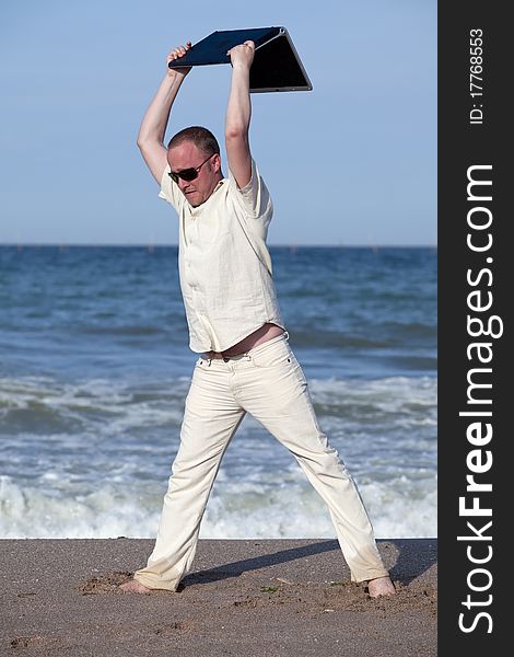 Sunburnt businessman at the beach throwing his laptop. Concept of protesting against work on vacation. Sunburnt businessman at the beach throwing his laptop. Concept of protesting against work on vacation