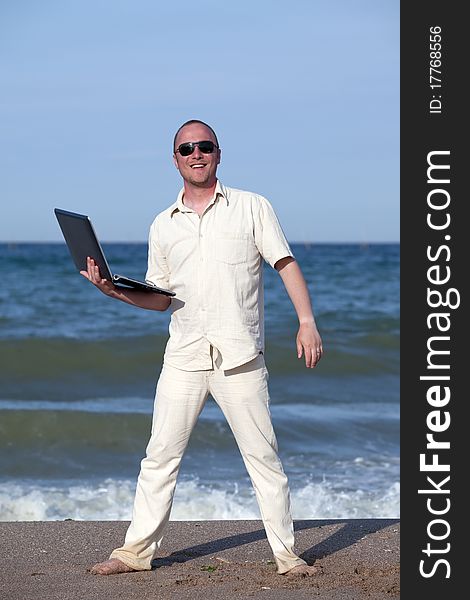 Young businessman at the beach with his laptop happy about success. Young businessman at the beach with his laptop happy about success