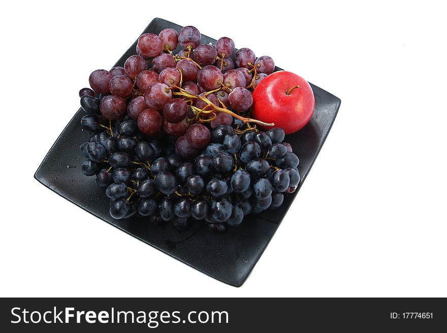 Two ripe clusters of grapes and one red apple lying on a black plate