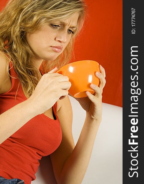 Young attractive woman sitting on the couch with a big orange cup. Staring into the mug with discontent and amazement. Young attractive woman sitting on the couch with a big orange cup. Staring into the mug with discontent and amazement