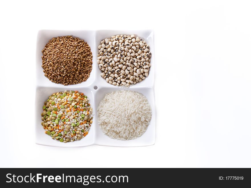 Four kinds of groats lie on a white plate on a white background. A shot horizontal, focus in the shot center.