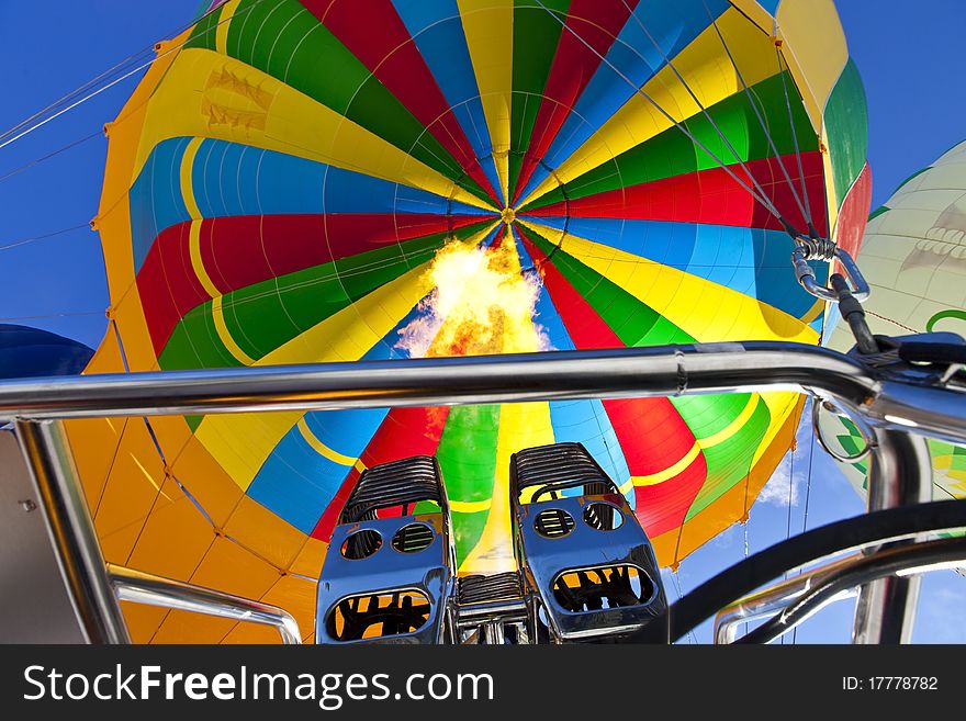 Photo of a colorful hot air balloon while he gets filled by flaming the air.
Two more balloons left and right.