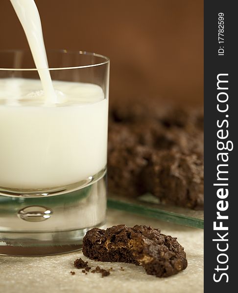 A delicious chocolate nut cookie with a bit out of it and a glass of milk being poured to go with it. A delicious chocolate nut cookie with a bit out of it and a glass of milk being poured to go with it.