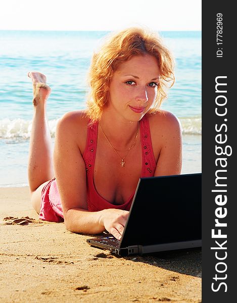 Nice redhead girl on the beach with a computer