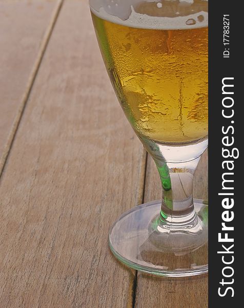 Glass of beer; closeup image of the beer in the elegant transparent glass, isolated on a wooden table, with space for text (copyspace) on the left side