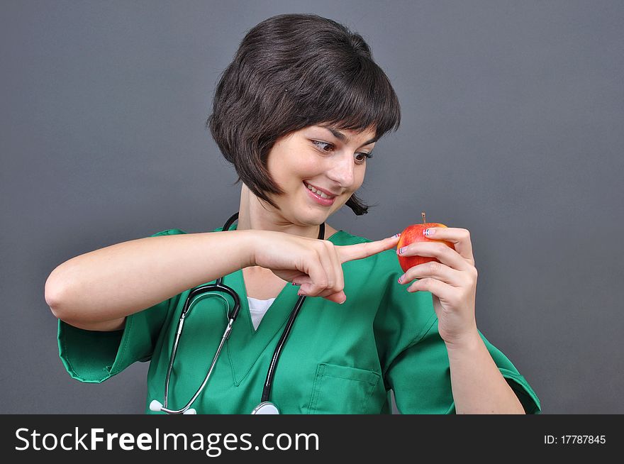 Attractive lady doctor with fresh apple on gray background