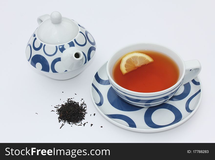 Cup of tea with teapot, crushed or loose tea leaves and a slice of lemon. Cup of tea with teapot, crushed or loose tea leaves and a slice of lemon