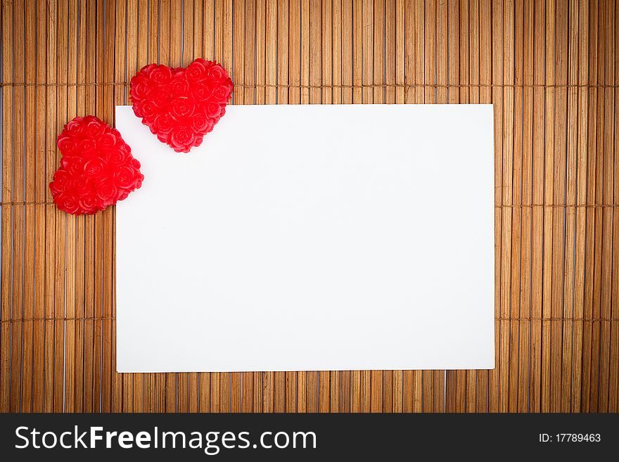 Two red hearts with paper card on wooden background