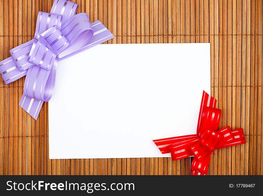 Violet and red bows with paper card on grunge wooden background