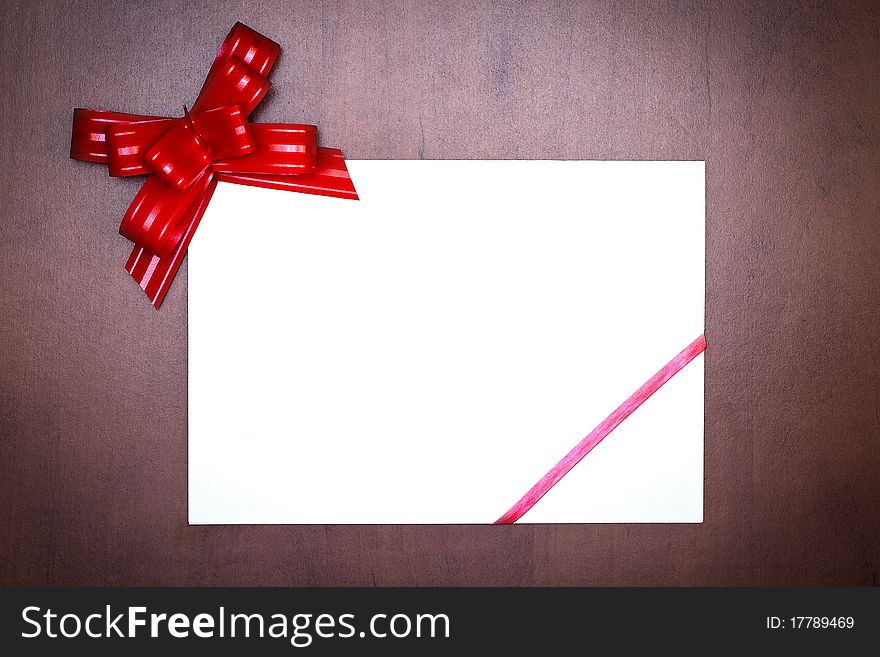 Red bow with paper card on grunge wooden background