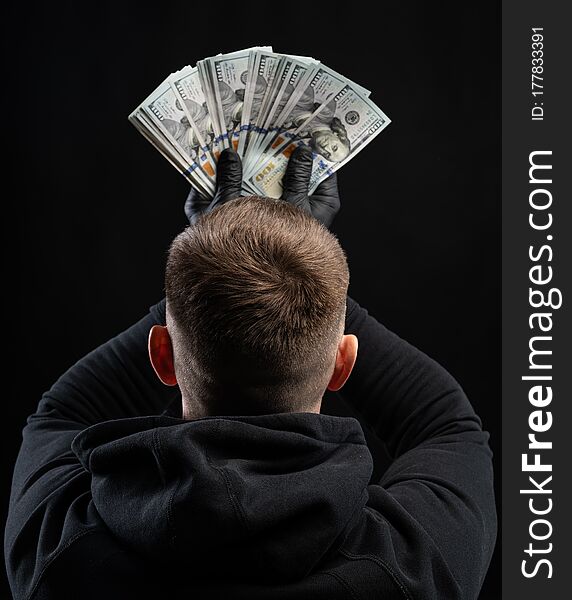 Business and finances concept. Man in black hoody holding pack of american dollars over black background
