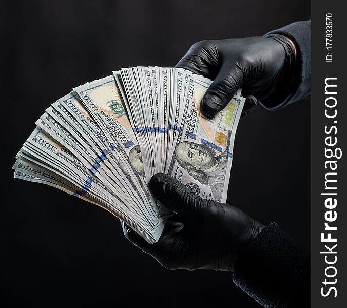Finances concept. Man in black gloves holding pack of dollars over black background