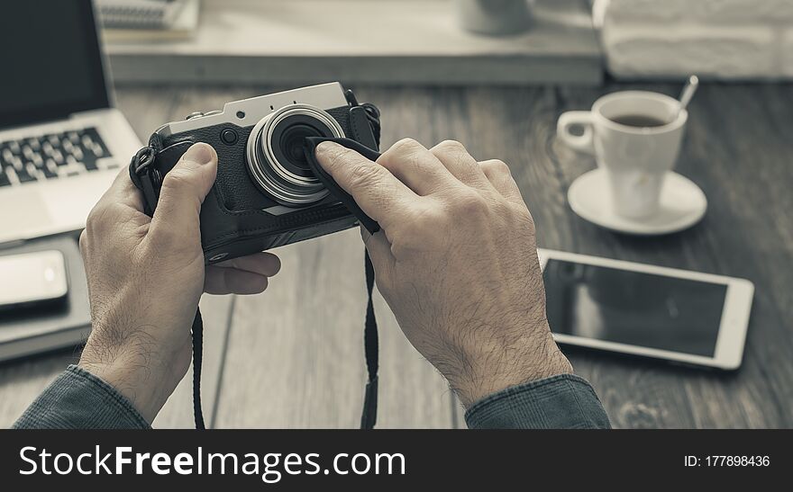 Hipster photographer at home sitting at desk and cleaning his camera lens with a cloth, point of view shot