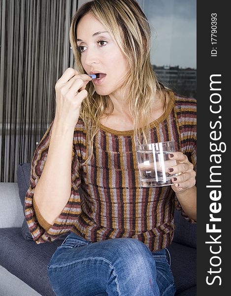 Blond woman taking a pill with a glass of water