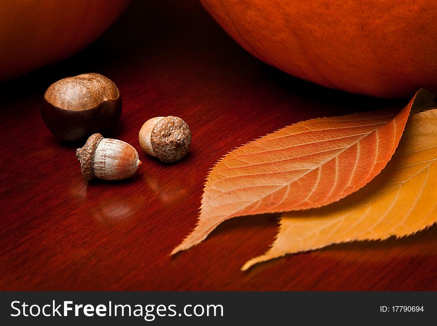 Two pumpkins, a chestnut, acorns and autumn leaves on a warm wooden table. Two pumpkins, a chestnut, acorns and autumn leaves on a warm wooden table.