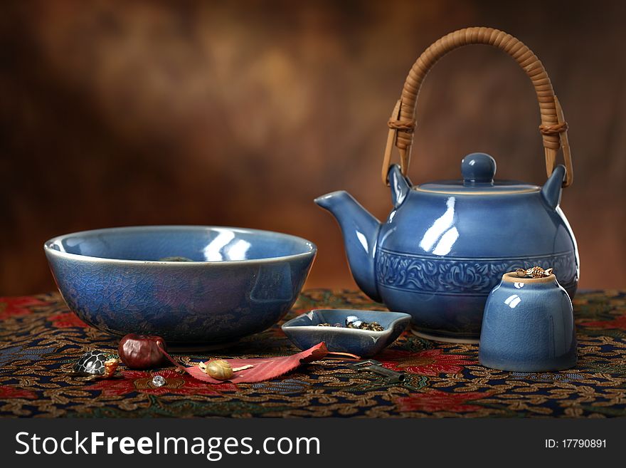 An Asian blue celedon teapot, bowl and cup along with various trinkets on a batik cloth with a sun beam in the background. An Asian blue celedon teapot, bowl and cup along with various trinkets on a batik cloth with a sun beam in the background.